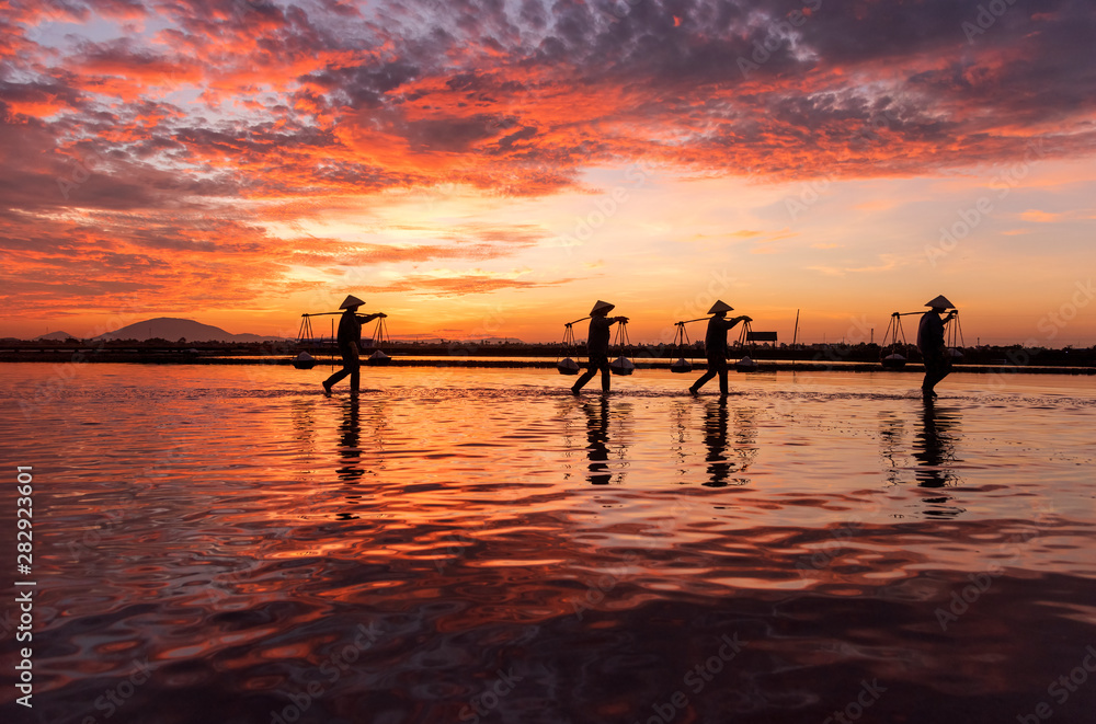 Woman carrying baskets of freshly harvested salt on their shoulders at sunrise in Hon Khoi salt field at sunrise, Nha Trang Province, Vietnam Woman carrying baskets of freshly harvested salt on their shoulders at sunrise in Hon Khoi salt field at sunrise, Nha Trang Province, Vietnam