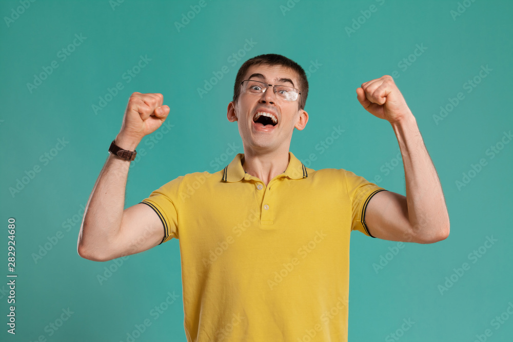 Fototapeta premium Handsome guy in a yellow casual t-shirt is posing over a blue background.