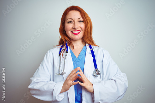 Young redhead doctor woman using stethoscope over white isolated background Hands together and fingers crossed smiling relaxed and cheerful. Success and optimistic
