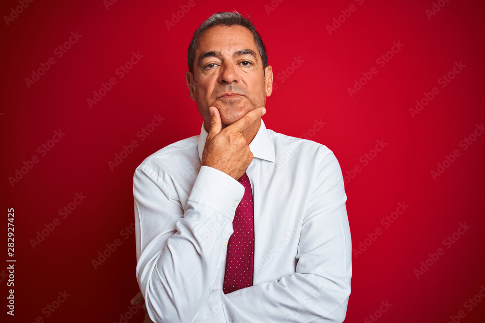 Handsome middle age businessman standing over isolated red background looking confident at the camera with smile with crossed arms and hand raised on chin. Thinking positive. Handsome middle age businessman standing over isolated red background looking confident at the camera with smile with crossed arms and hand raised on chin. Thinking positive.