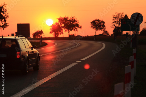 Samochód osobowy na tle zachodzącego słońca.