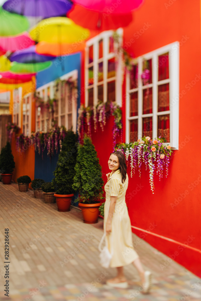 Obraz premium Travel tourist brunette woman in yellow dress walks the streets with bright decoration of the city. Tilt-shift lens blur