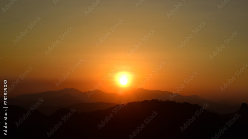 sun setting behind a dense forest area followed by mountains.