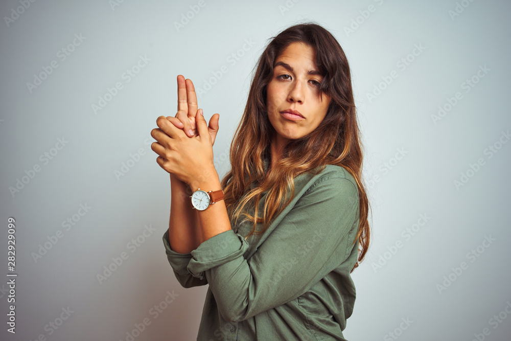 Young beautiful woman wearing green shirt standing over grey isolated background Holding symbolic gun with hand gesture, playing killing shooting weapons, angry face Young beautiful woman wearing green shirt standing over grey isolated background Holding symbolic gun with hand gesture, playing killing shooting weapons, angry face