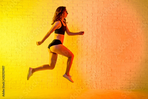 Young athletic woman jumping over a yellow background.