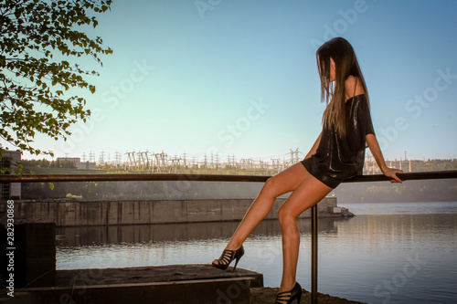 Young woman in the cute summer dress sitting on the pier looking at sunset © Сергей Курбатов