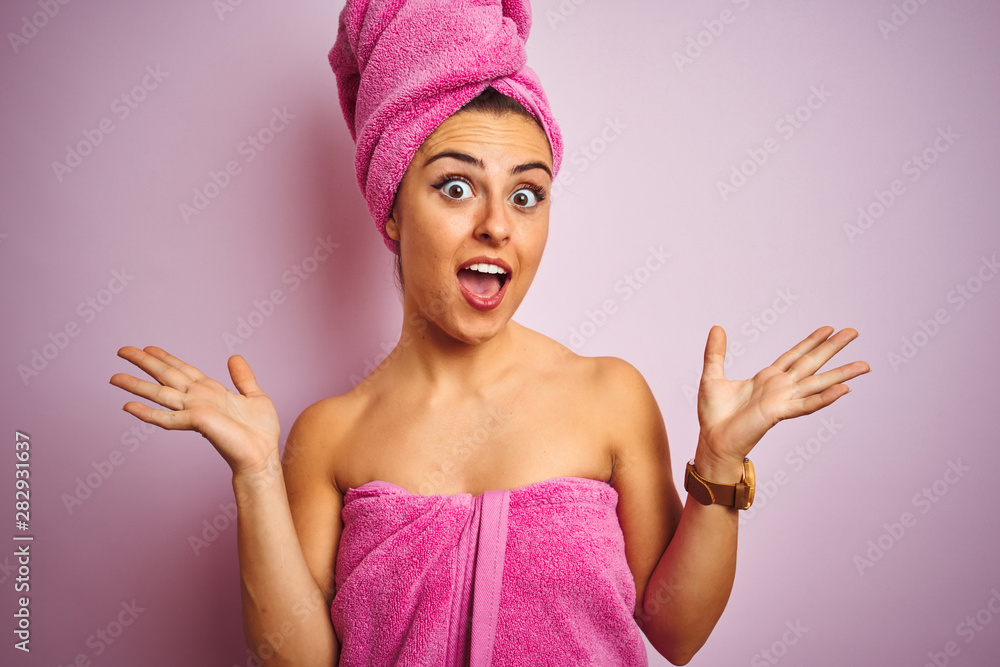 Young beautiful woman wearing towel after shower over isolated pink background celebrating crazy and amazed for success with arms raised and open eyes screaming excited. Winner concept Young beautiful woman wearing towel after shower over isolated pink background celebrating crazy and amazed for success with arms raised and open eyes screaming excited. Winner concept