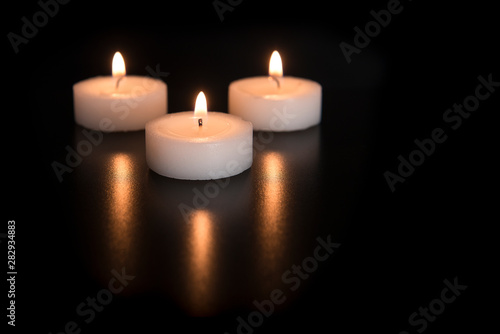 Three burning tea lights with their reflection on a black background