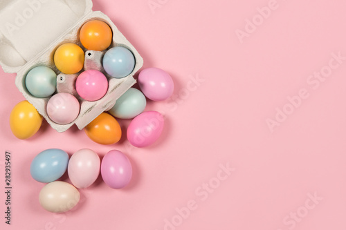 Easter background with a carton egg box with pastel colored easter eggs in and beside it on a pink background with space for copy