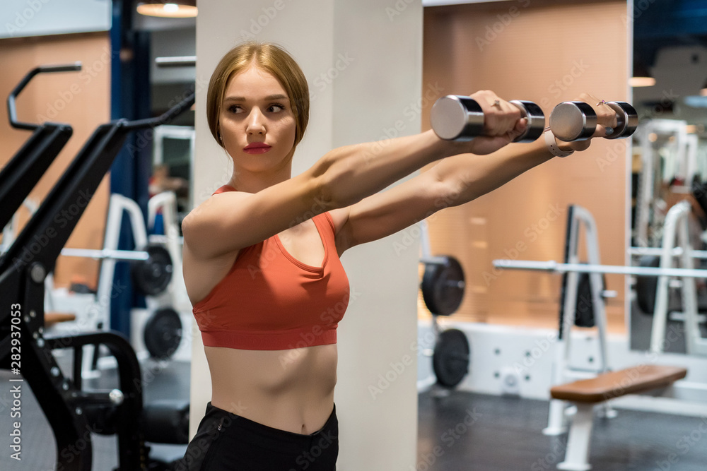 Beautiful young woman trains deltoid in gym Beautiful young woman trains deltoid in gym