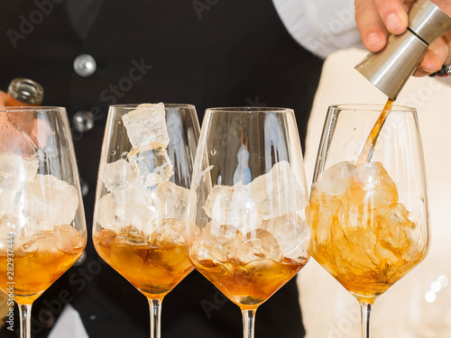 The bartender cooks alcoholic cocktail. On a bar counter 4 glasses with ice and whisky. The moment of adding of ingradiyent from a measured bowl in a glass