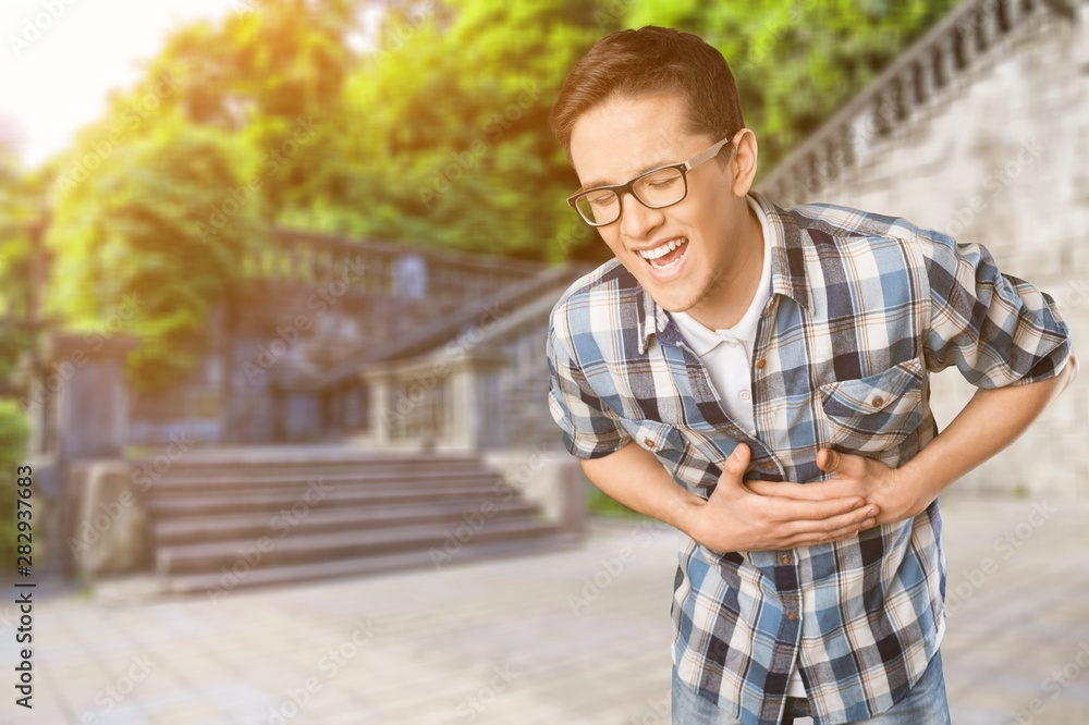 Obraz premium Man laughing and holding stomach on grey wall background