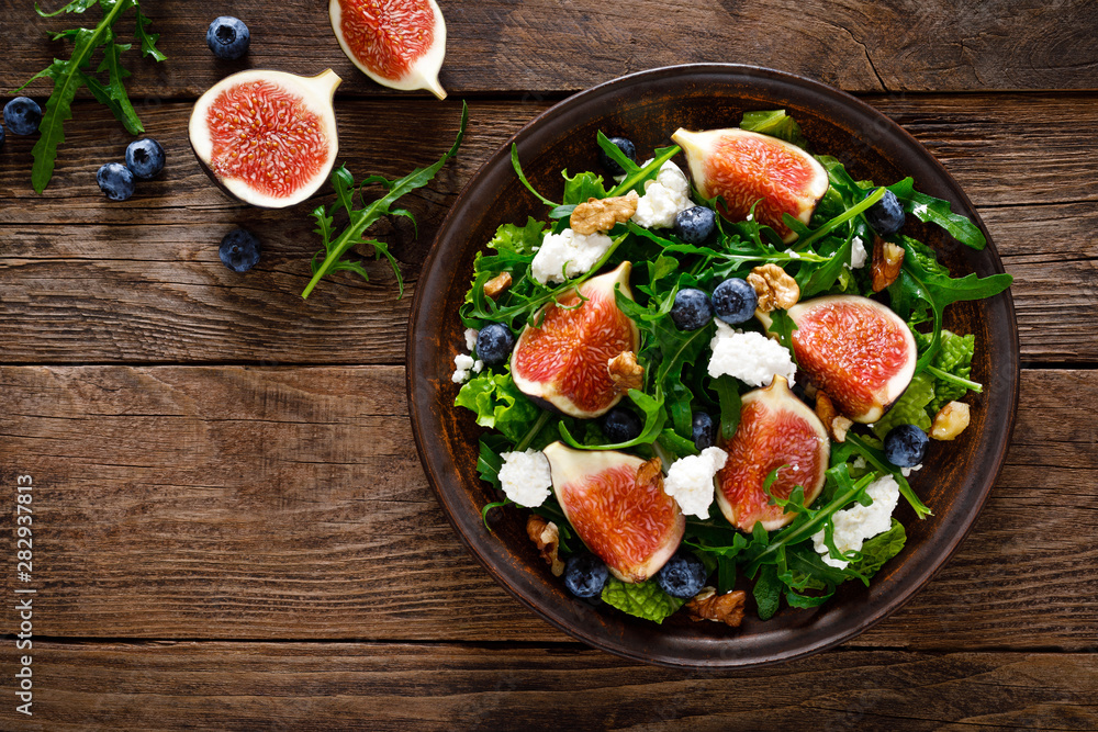 Fig salad with goat cheese, blueberry, walnuts and arugula on wooden background. Healthy food. Top view Fig salad with goat cheese, blueberry, walnuts and arugula on wooden background. Healthy food. Top view