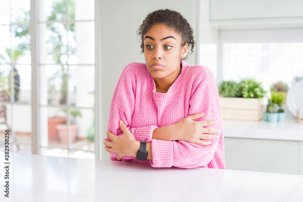 Beautiful african american woman with afro hair wearing casual pink sweater shaking and freezing for winter cold with sad and shock expression on face Beautiful african american woman with afro hair wearing casual pink sweater shaking and freezing for winter cold with sad and shock expression on face