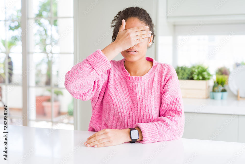 Beautiful african american woman with afro hair wearing casual pink sweater covering eyes with hand, looking serious and sad. Sightless, hiding and rejection concept