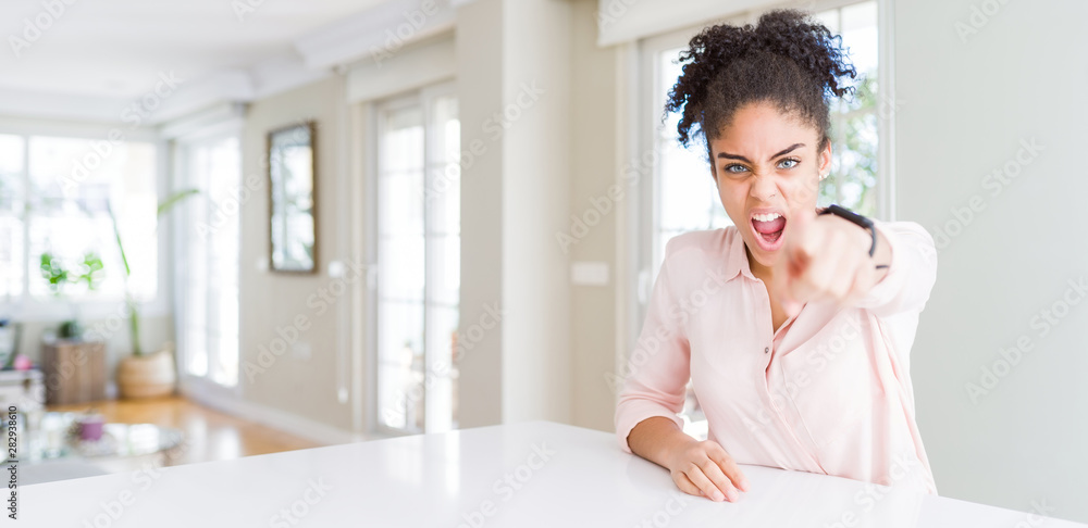 Wide angle of beautiful african american woman with afro hair pointing displeased and frustrated to the camera, angry and furious with you Wide angle of beautiful african american woman with afro hair pointing displeased and frustrated to the camera, angry and furious with you