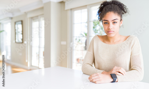 Beautiful young african american woman with afro hair sitting on table at home skeptic and nervous, frowning upset because of problem. Negative person.