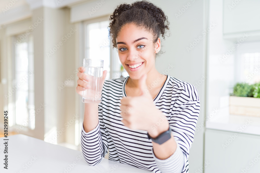 Young african american girl drinking a fresh glass of water happy with big smile doing ok sign, thumb up with fingers, excellent sign Young african american girl drinking a fresh glass of water happy with big smile doing ok sign, thumb up with fingers, excellent sign