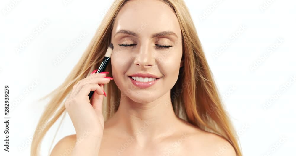 Beautiful blonde female stroking face and neck skin with makeup brush and looking to camera isolated on white background, closeup Beautiful blonde female stroking face and neck skin with makeup brush and looking to camera isolated on white background, closeup