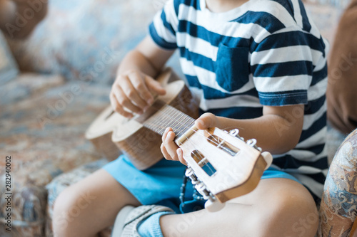  Caucasian child playing and making music chords with small guitar or ukulele, close up