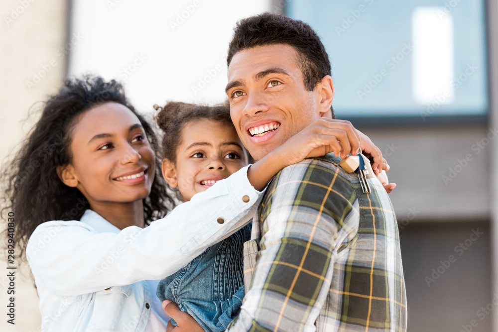 Obraz premium family hugging and looking away while african american woman holding key and man holding daughter