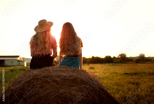 girls with long hairs sitting on a haystack and enjoying summer sunset. International Children’s Day concept. friendship and love