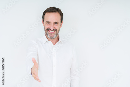 Elegant senior man over isolated background smiling friendly offering handshake as greeting and welcoming. Successful business.