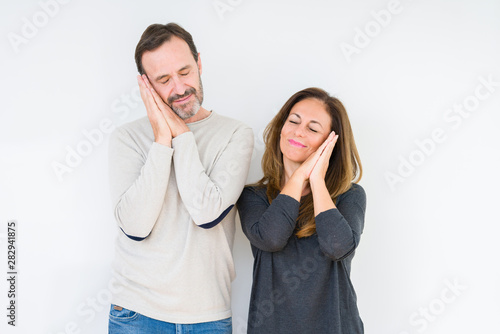 Beautiful middle age couple in love over isolated background sleeping tired dreaming and posing with hands together while smiling with closed eyes.