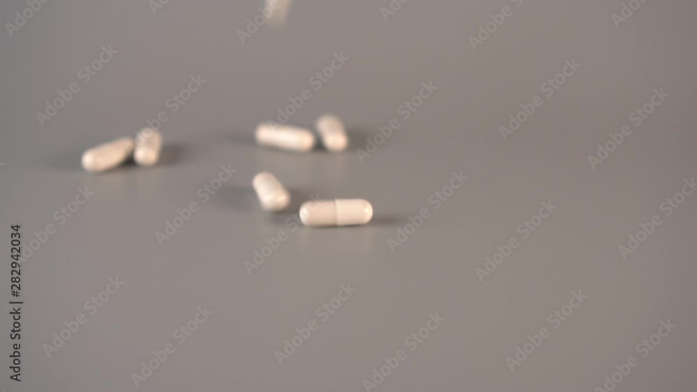 White medical capsules fall from above on a gray table. The concept of the use of homeopathic remedies. Slow motion White medical capsules fall from above on a gray table. The concept of the use of homeopathic remedies. Slow motion