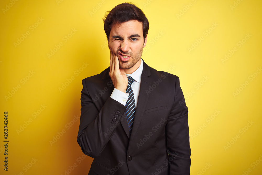 Young handsome businessman wearing suit and tie standing over isolated yellow background touching mouth with hand with painful expression because of toothache or dental illness on teeth. Young handsome businessman wearing suit and tie standing over isolated yellow background touching mouth with hand with painful expression because of toothache or dental illness on teeth.