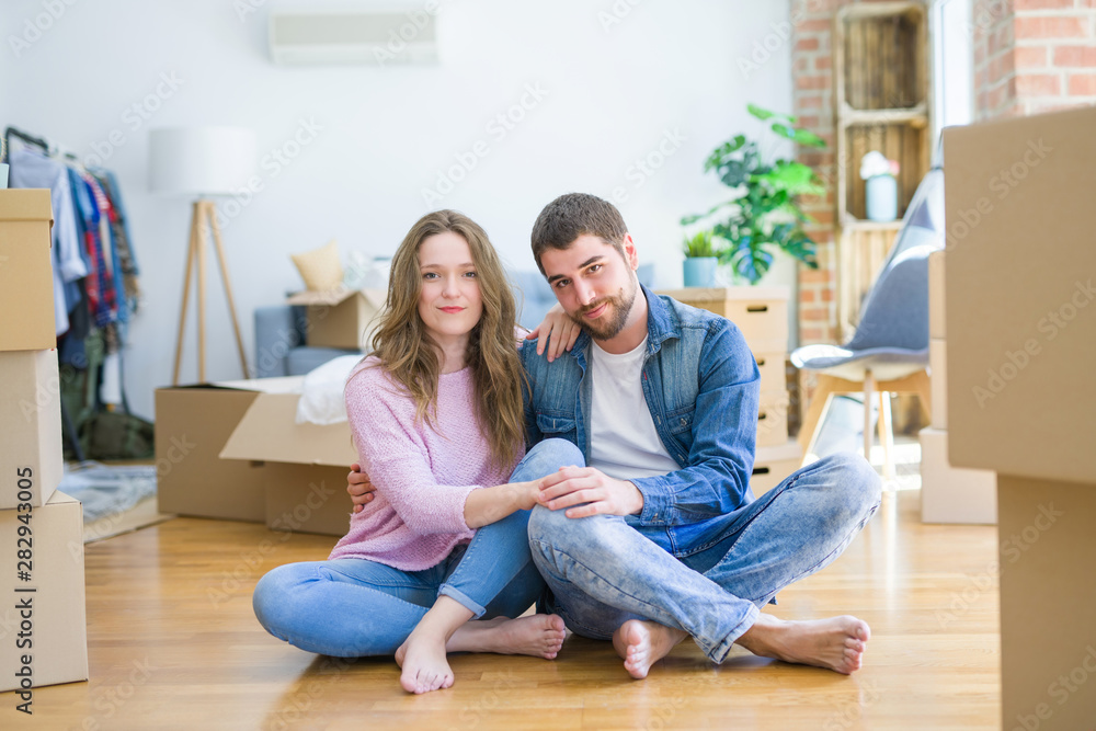 Young beautiful couple moving to a new house sitting on the floor with serious expression on face. Simple and natural looking at the camera. Young beautiful couple moving to a new house sitting on the floor with serious expression on face. Simple and natural looking at the camera.