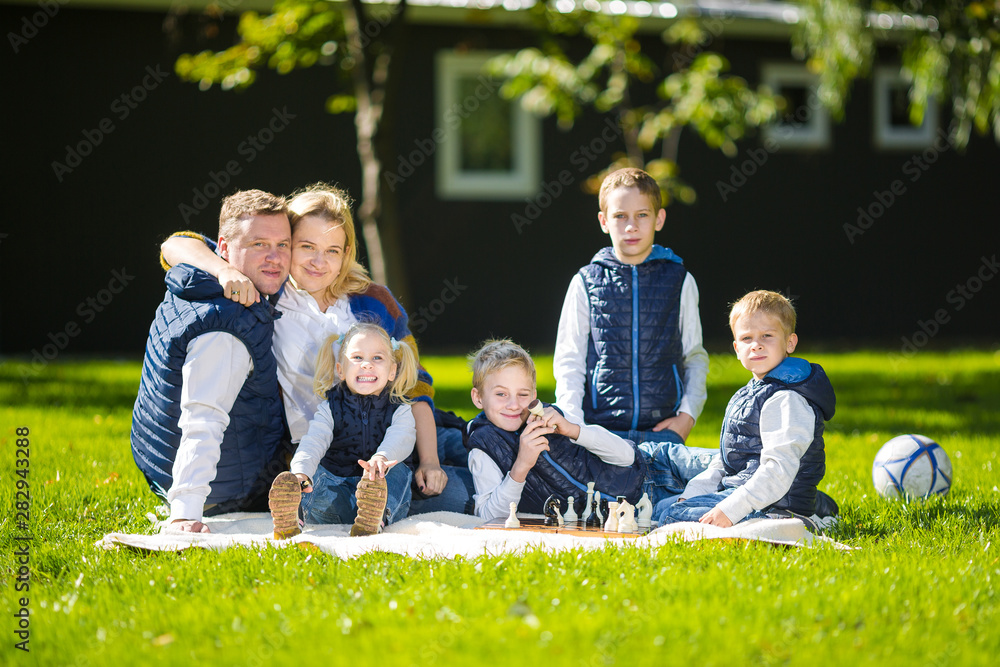 Fototapeta premium Big Family Relaxing In Green Nature. Happy family portrait on outdoor, group six people sit on grass, summer season, child and parent. Children, parenthood and nature concept. picnic outdoors on lawn
