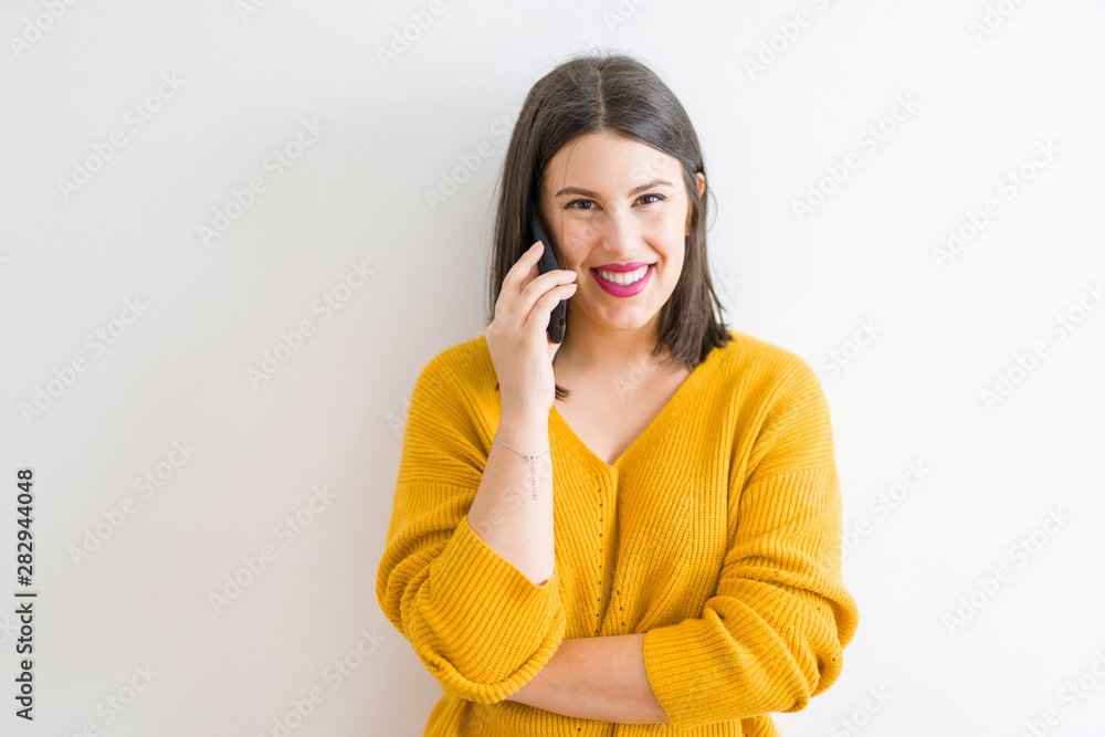 Beautiful brunette young woman smiling confident calling using smartphone over isolated white background wearing casual yellow sweater Beautiful brunette young woman smiling confident calling using smartphone over isolated white background wearing casual yellow sweater