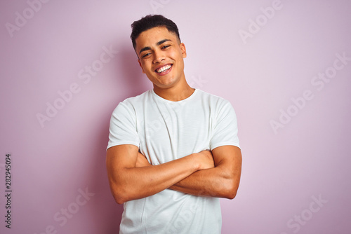 Young brazilian man wearing t-shirt standing over isolated pink background happy face smiling with crossed arms looking at the camera. Positive person.