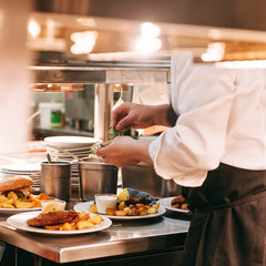 Food orders on the kitchen table in the restaurant, chief decorating schnitzel and fried potatoes, traditional german plate