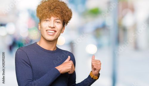Young handsome man with afro hair Pointing to the back behind with hand and thumbs up, smiling confident photo