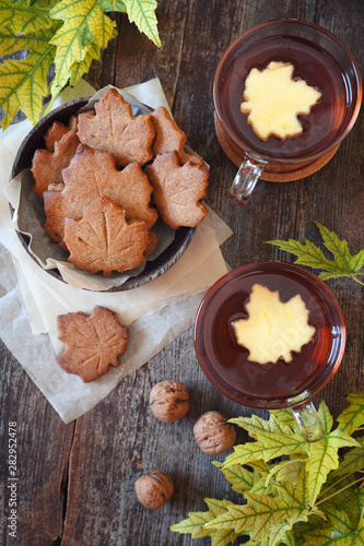Autumn mood: cinnamon cookies in form of maple leaves, two cups of tea and yellow leaves