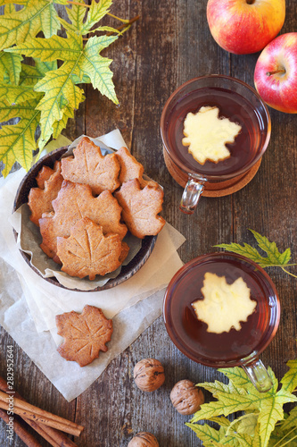 Autumn mood: cinnamon cookies in form of maple leaves, two cups  of tea, red apples and yellow leaves