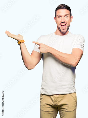 Handsome man wearing casual white t-shirt amazed and smiling to the camera while presenting with hand and pointing with finger.