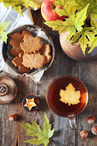 Autumn mood: cinnamon cookies in form of maple leaves, cup of tea, red apple and yellow leaves