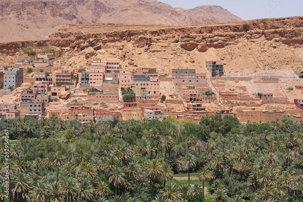 Landscape with an ancient town Tinghir, a beautiful lush Green Oasis and palm grove surrounded by rocky Atlas Mountains at Todra Gorge in southeastern Morocco, North Africa. Old Berber Architecture.