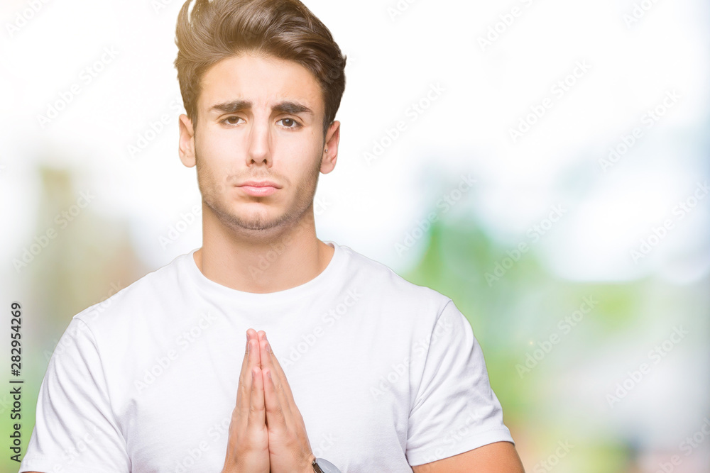 Young handsome man wearing white t-shirt over isolated background begging and praying with hands together with hope expression on face very emotional and worried. Asking for forgiveness. Young handsome man wearing white t-shirt over isolated background begging and praying with hands together with hope expression on face very emotional and worried. Asking for forgiveness.