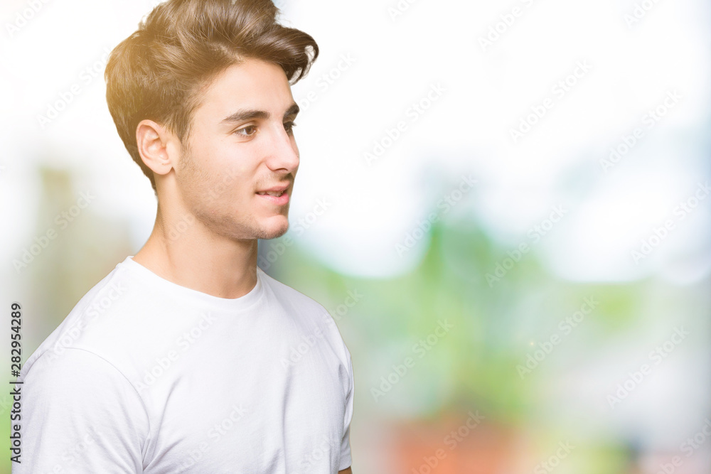Young handsome man wearing white t-shirt over isolated background looking away to side with smile on face, natural expression. Laughing confident. Young handsome man wearing white t-shirt over isolated background looking away to side with smile on face, natural expression. Laughing confident.