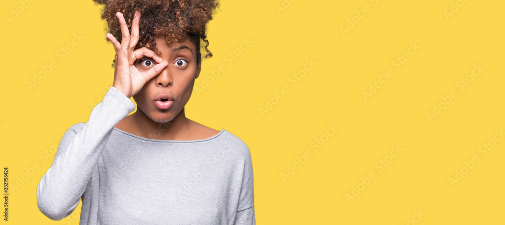 Beautiful young african american woman over isolated background doing ok gesture shocked with surprised face, eye looking through fingers. Unbelieving expression. - obrazy, fototapety, plakaty 