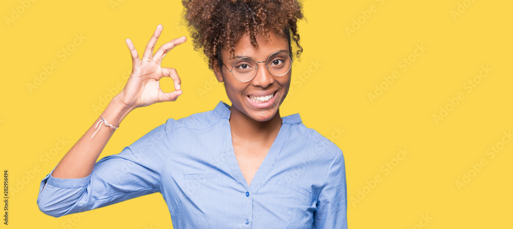 Beautiful young african american business woman over isolated background smiling positive doing ok sign with hand and fingers. Successful expression. - obrazy, fototapety, plakaty 