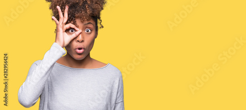 Beautiful young african american woman over isolated background doing ok gesture shocked with surprised face, eye looking through fingers. Unbelieving expression.