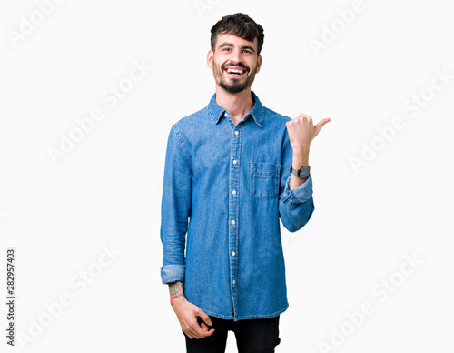 Young handsome man over isolated background smiling with happy face looking and pointing to the side with thumb up.
