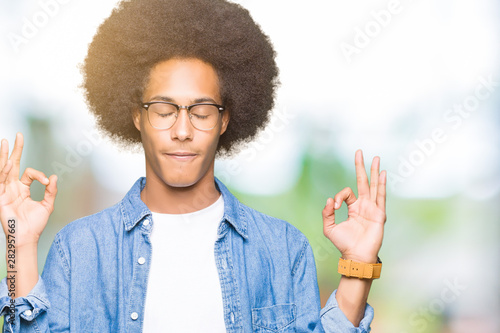 Young african american man with afro hair wearing glasses relax and smiling with eyes closed doing meditation gesture with fingers. Yoga concept.