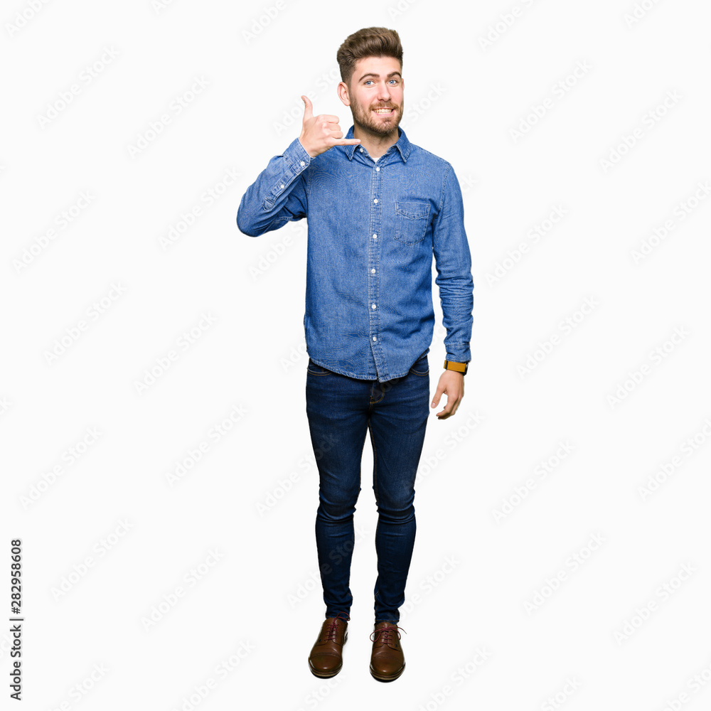 Young handsome blond man wearing casual denim shirt smiling doing phone gesture with hand and fingers like talking on the telephone. Communicating concepts. Young handsome blond man wearing casual denim shirt smiling doing phone gesture with hand and fingers like talking on the telephone. Communicating concepts.