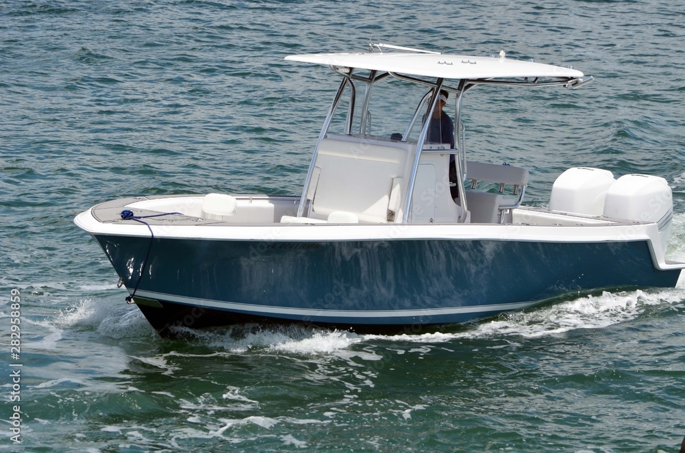 Small open blue and white fishing boat with white fiberglass canopy powered by two outboard engines Small open blue and white fishing boat with white fiberglass canopy powered by two outboard engines